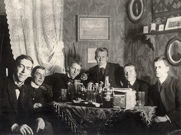 Historisk svarthvitt bilde av en gruppe unge menn som sitter rundt et bord.