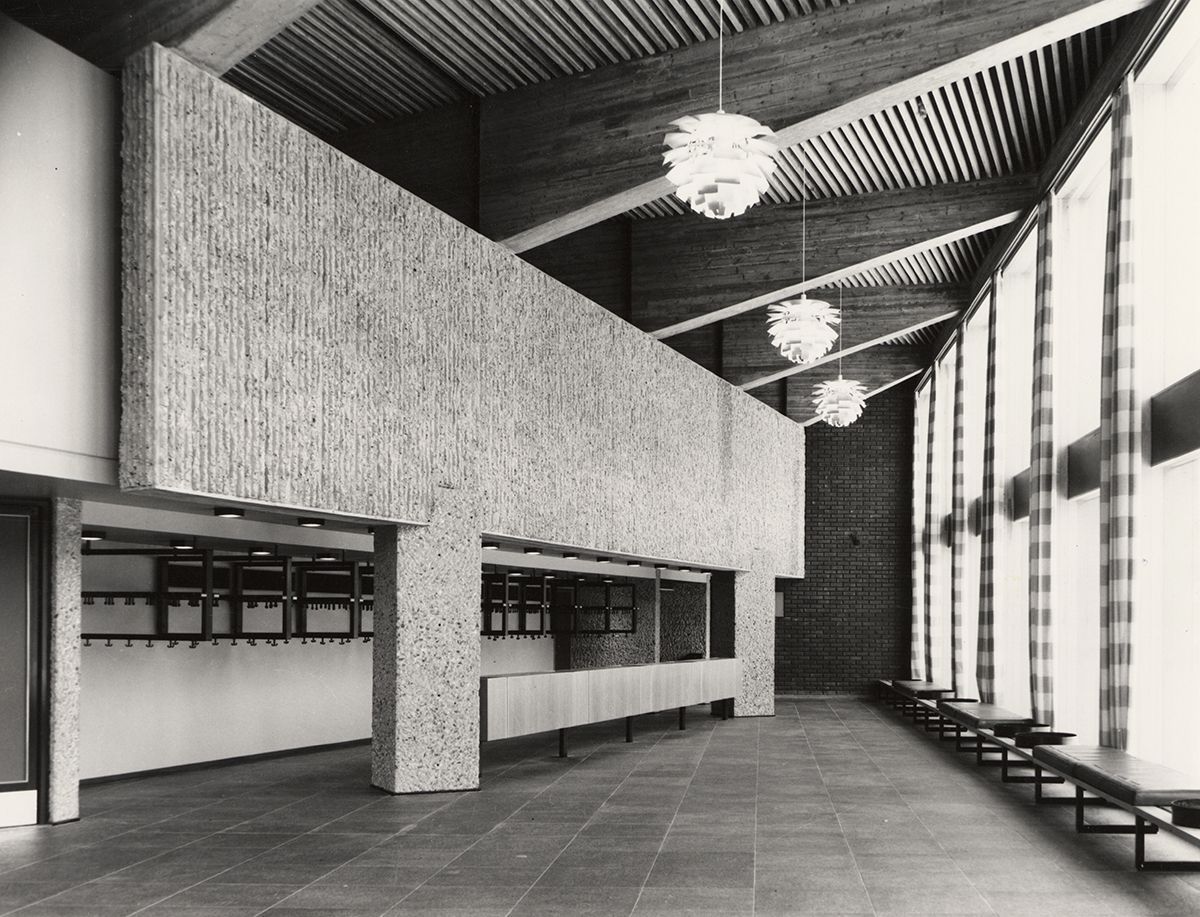 Sophus Lies Auditorium var opprinnelig Blinderns største. Vestibylen har garderobe&amp;#160;med skranke langs innerveggene og benker med skaikledde puter langs vinduene. Her i Matematikkomplekset introduserer Leif Olav Moen en ny betongteknikk på Blindern, Rudolphbetong. Den er en videreutvikling av naturbetongen vi kjenner fra SV-bygningene og uteområdene, oppkalt etter den amerikanske arkitekten Paul Rudolph. I 1962 tok han i bruk en egen teknikk med&amp;#160;ribber av tre inne i forskalingene. De&amp;#160;ferdige betongelementene&amp;#160;fikk slik riflede flater. I denne vestibylen ser vi også dragere av upusset betong og himling av treribber. I taket henger innkjøpte lysarmaturer, den danske arkitekten Poul Henningsens &quot;Konglen&quot; (1958)&amp;#160;eller &quot;PH Artichoke&quot;, som er den internasjonale betegnelsen.&amp;#160;
1966-1968. Fotograf: Teigens fotoatelier.&amp;#160;