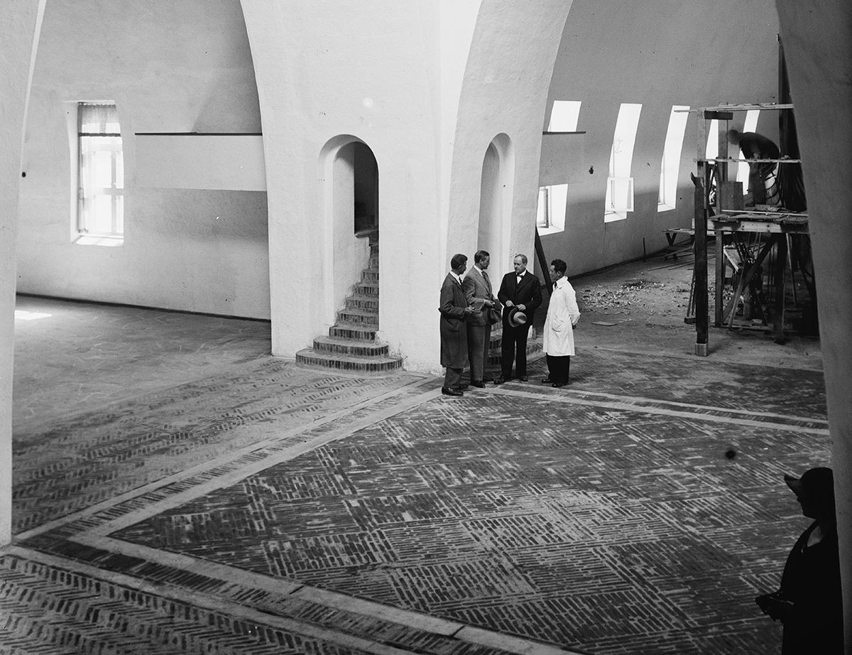 Professor A.W. Brøgger står i samtale foran Gokstadskipet. Legg merke til det vakre gulvet, hvor tegl er lagt i mønster etter inspirasjon fra middelalderens teglgulv.&amp;#160;
1932. Fotograf: Henriksen &amp;#38; Steen/Nasjonalbiblioteket.&amp;#160;